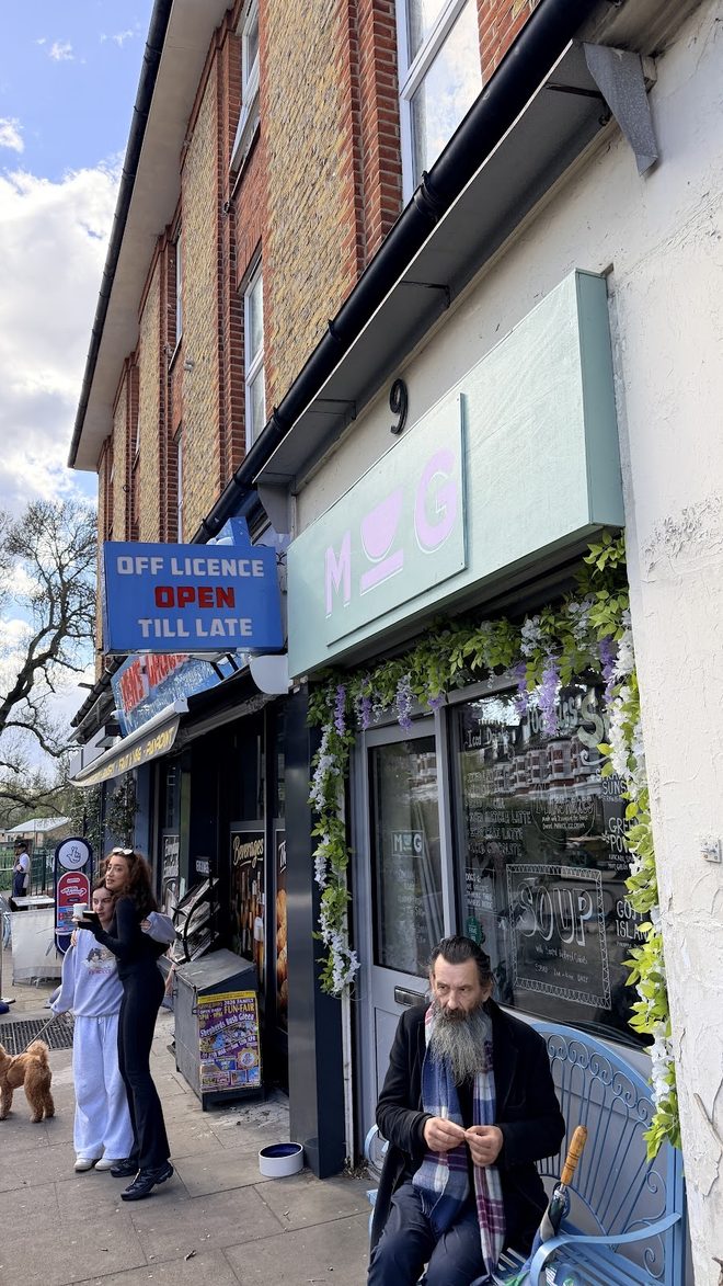 Street-level view of the MUG shopfront on the brick parade, people and a dog passing