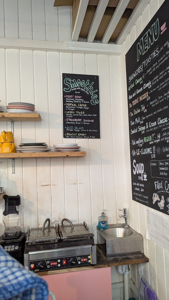 The service area behind the counter with panini press, sink and open shelving