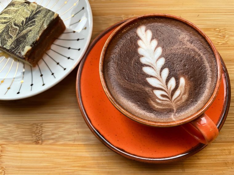 Mocha with leaf latte art and a slice of marbled brownie on a wooden board